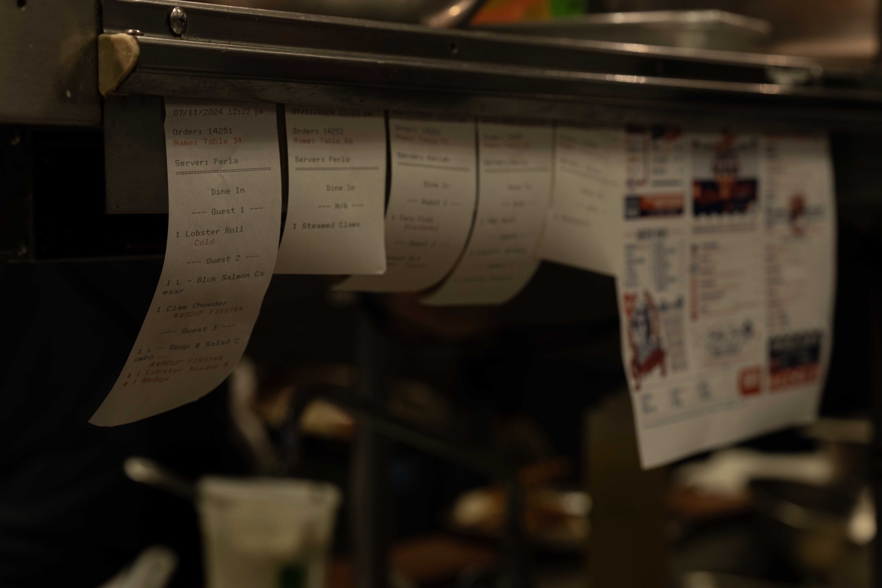 Order tickets lined up along the kitchen expo rail during service
